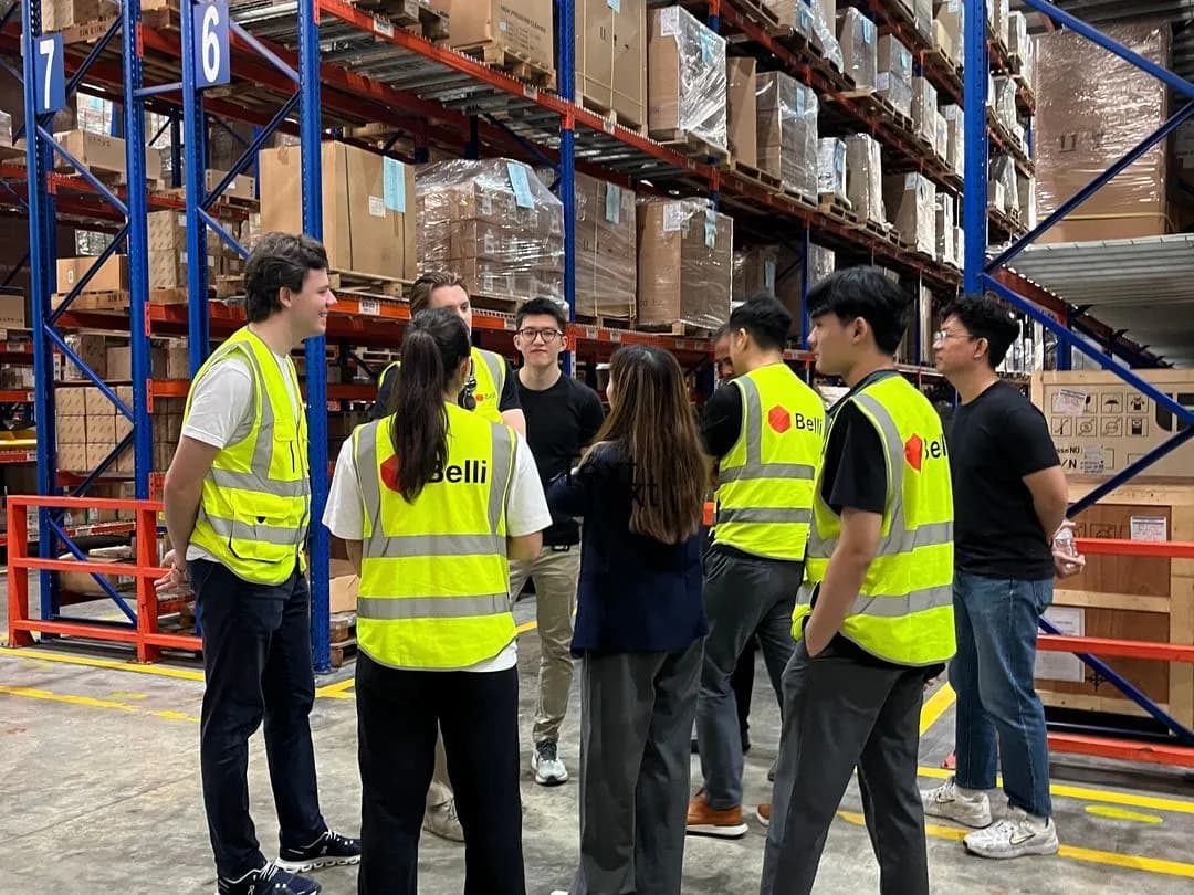 Associates in Belli hi-vis in a huddle between warehouse racking