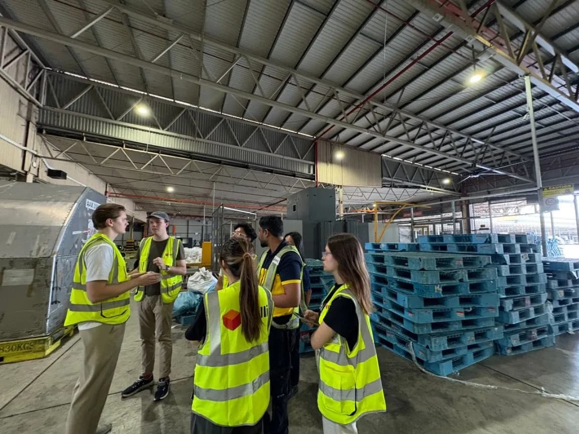 Belli and airline staff in high-visibility vests beside a stack of pallets in a cargo warehouse